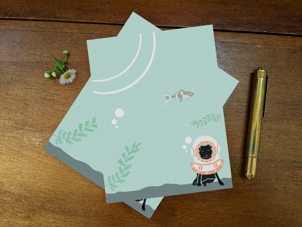 Notepad with a dog with old school diving helmet on a wooden surface and gold pen.