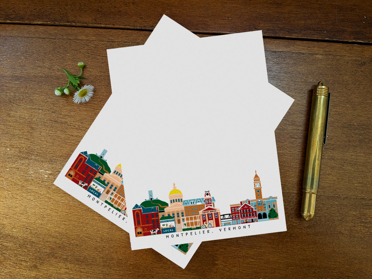 Notepad pages with illustration of Montpelier, Vermont buildings in skyline on a wood surface and gold pen