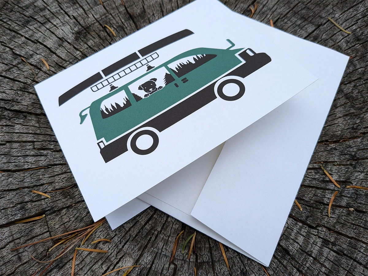 Greeting card with image of dog riding in a camper van with canoe on top.