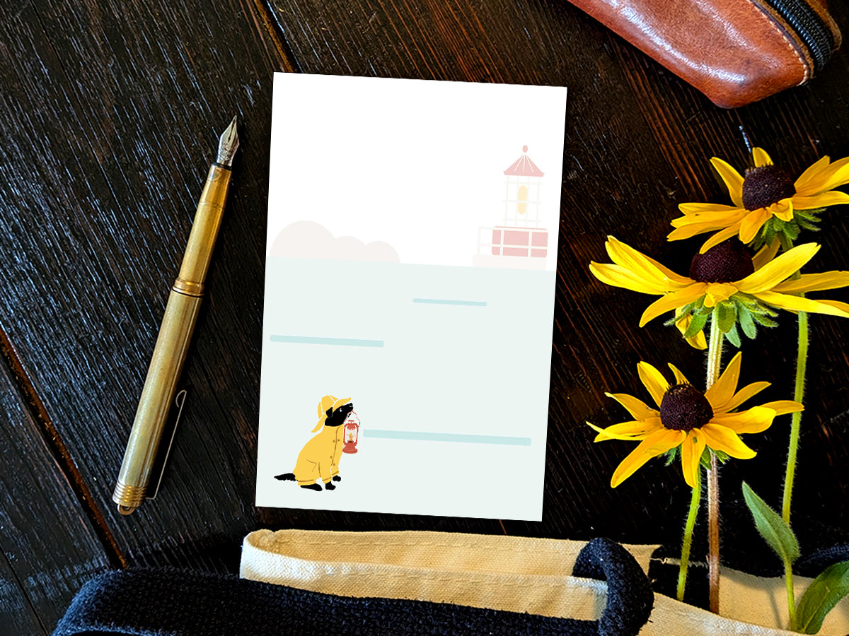 Notepad with an illustration of a dog in yellow hat and jacket holding a red lantern with a lighthouse in the background, placed on a wood surface with a gold pen, and yellow flowers.