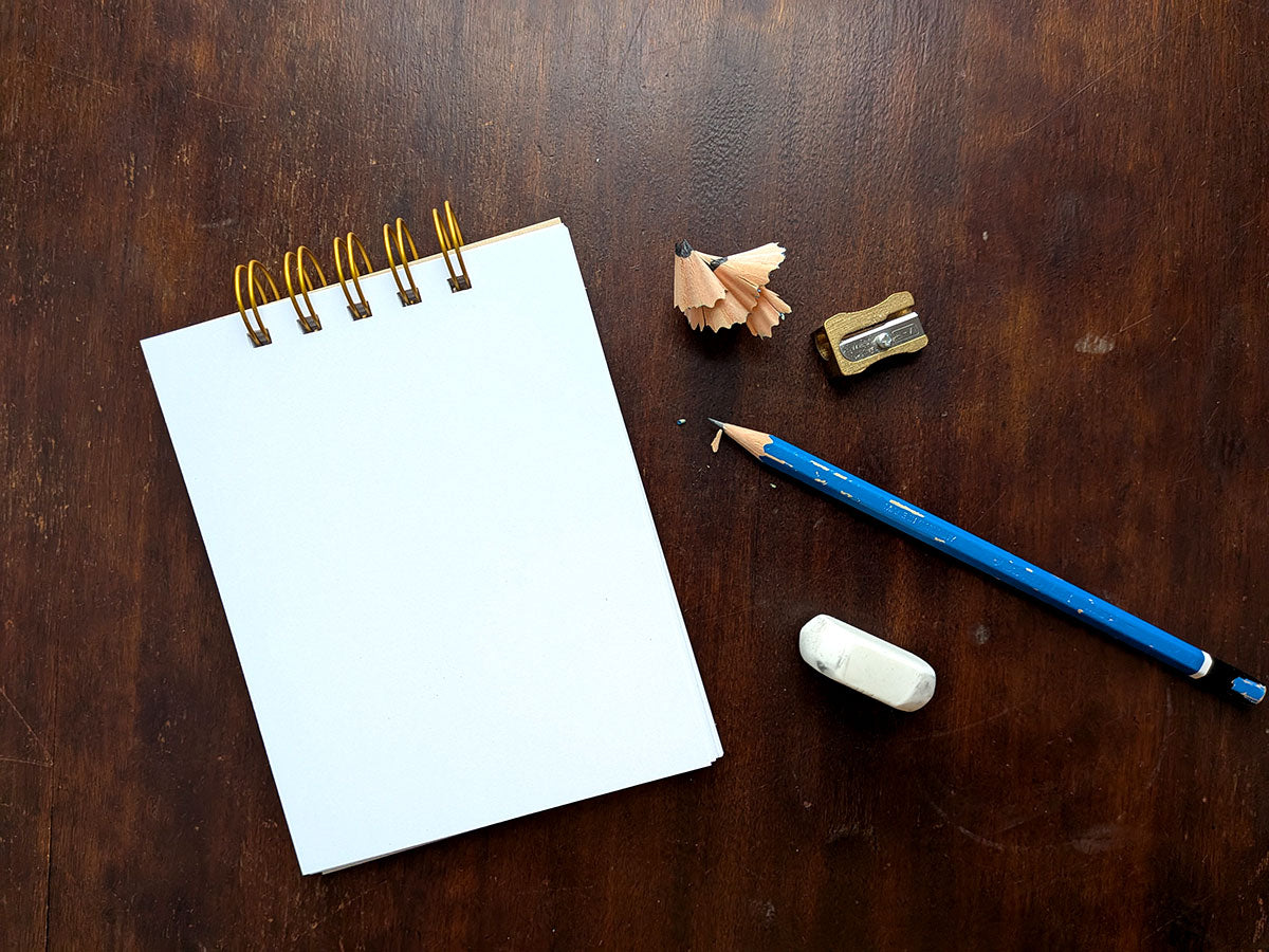 Notebook with a blue pencil, eraser, and sharpener on a wooden surface