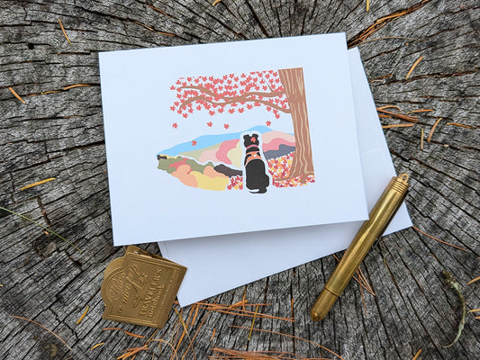 Greeting card with image of black dog underneath a maple tree with red fall foliage and mountains in the background.