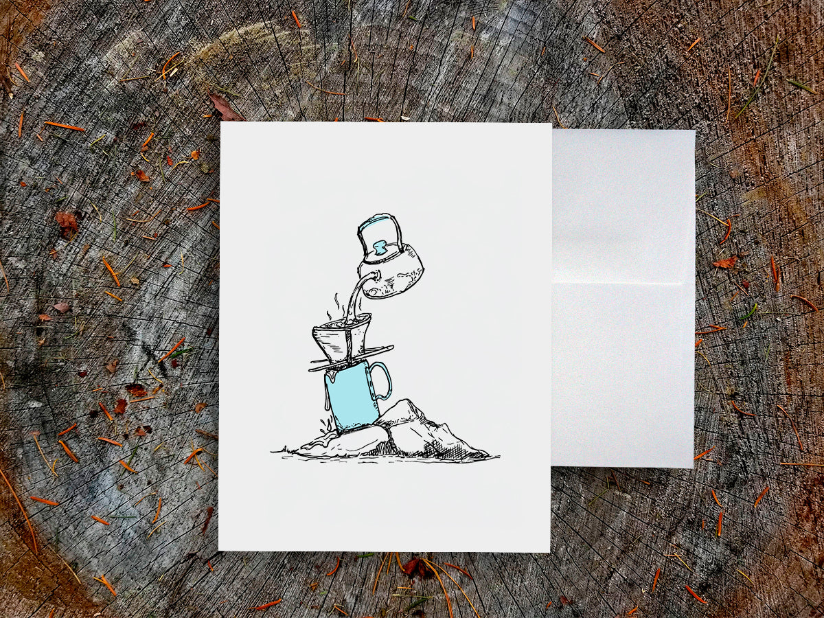White card with a black ink drawing of pour-over coffee on a wooden surface.