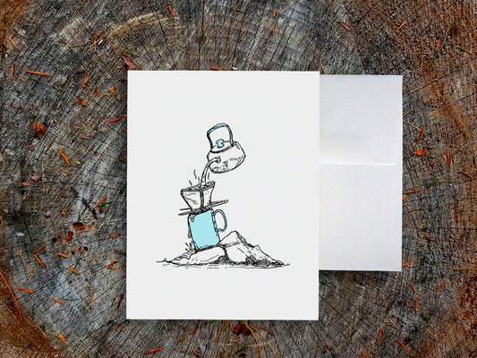 White card with a black ink drawing of pour-over coffee on a wooden surface.