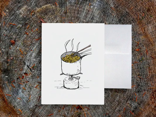 White card with a black ink drawing of a pot of ramen over a camp stove on a wooden surface.