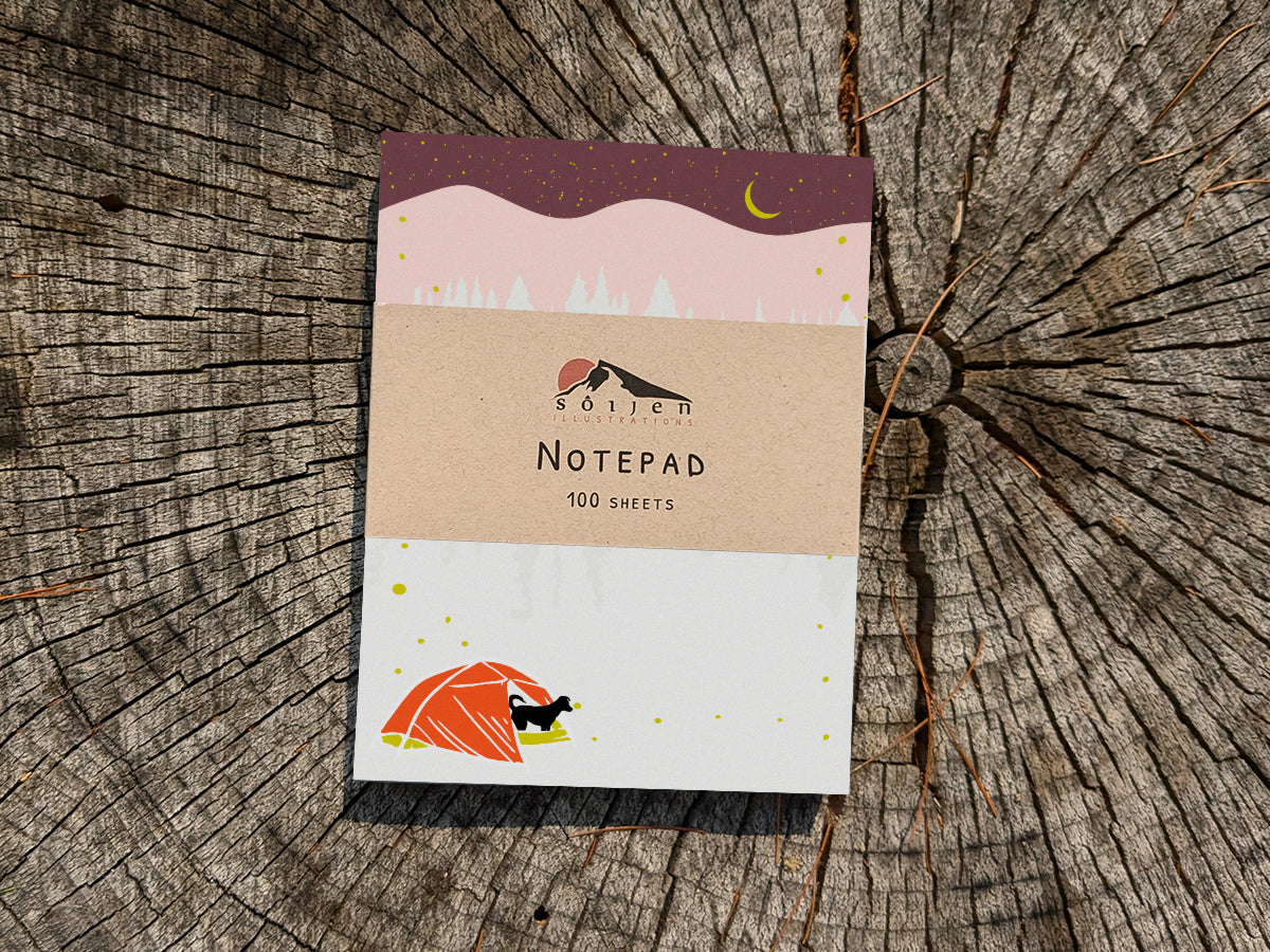 Notepad with a black dog in red tent and night sky on wooden background.