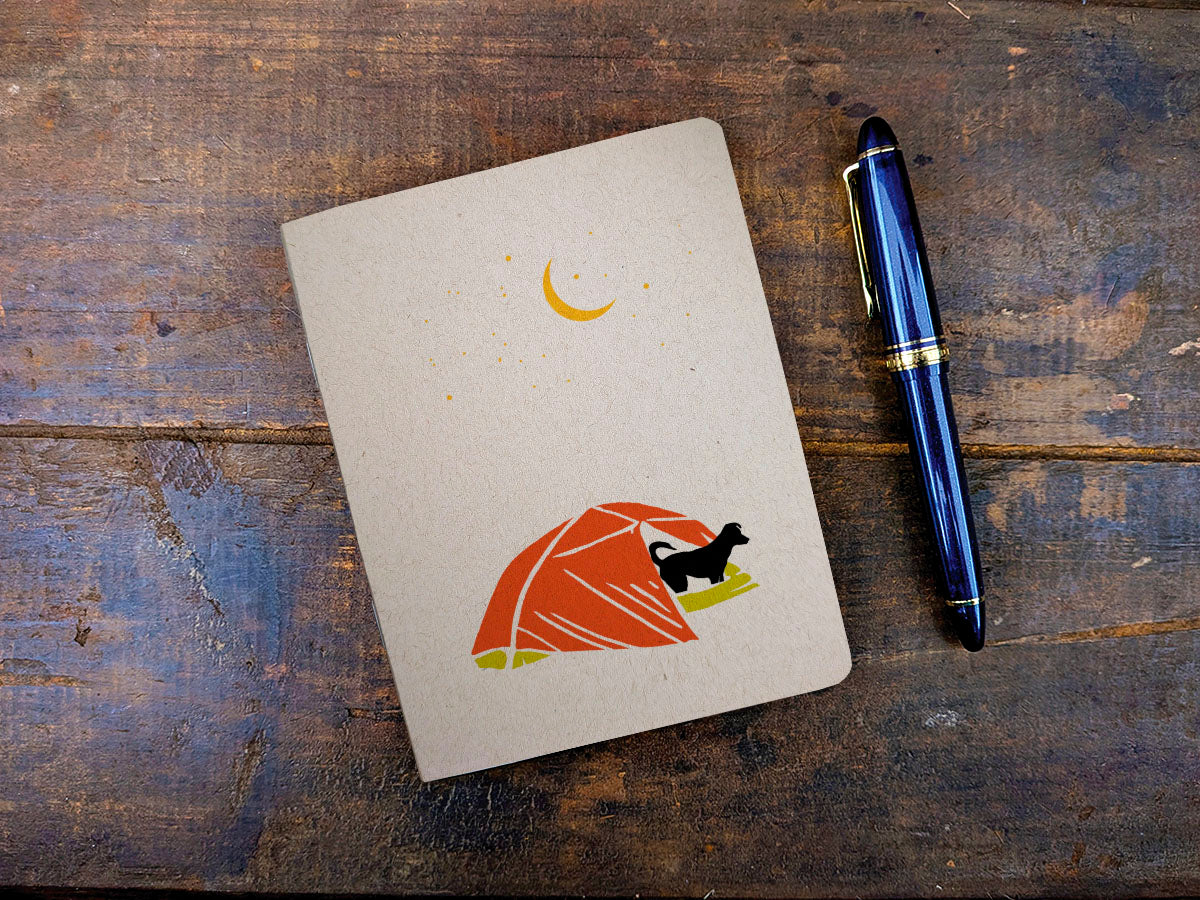 Notebook with a dog camping illustration and a pen on a wooden surface