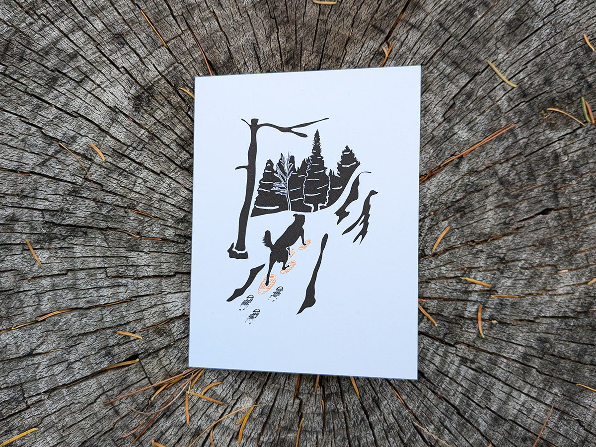 Greeting card with image of dog walking through forest wearing yellow snowshoes.