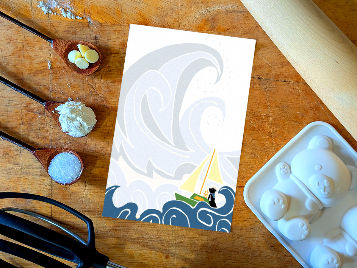 Notepad with illustration of dog sailing big waves on a wood surface with baking supplies.