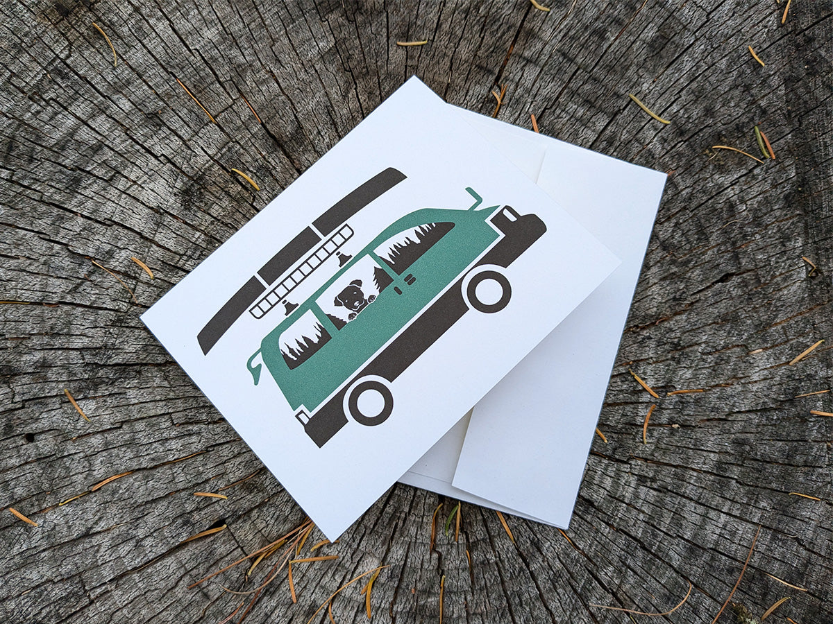 Greeting card with image of dog riding in a camper van with canoe on top.