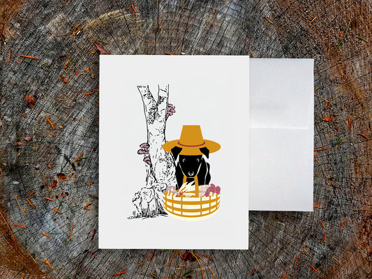 White card with drawing of dog holding basket with mushrooms on a wooden surface.