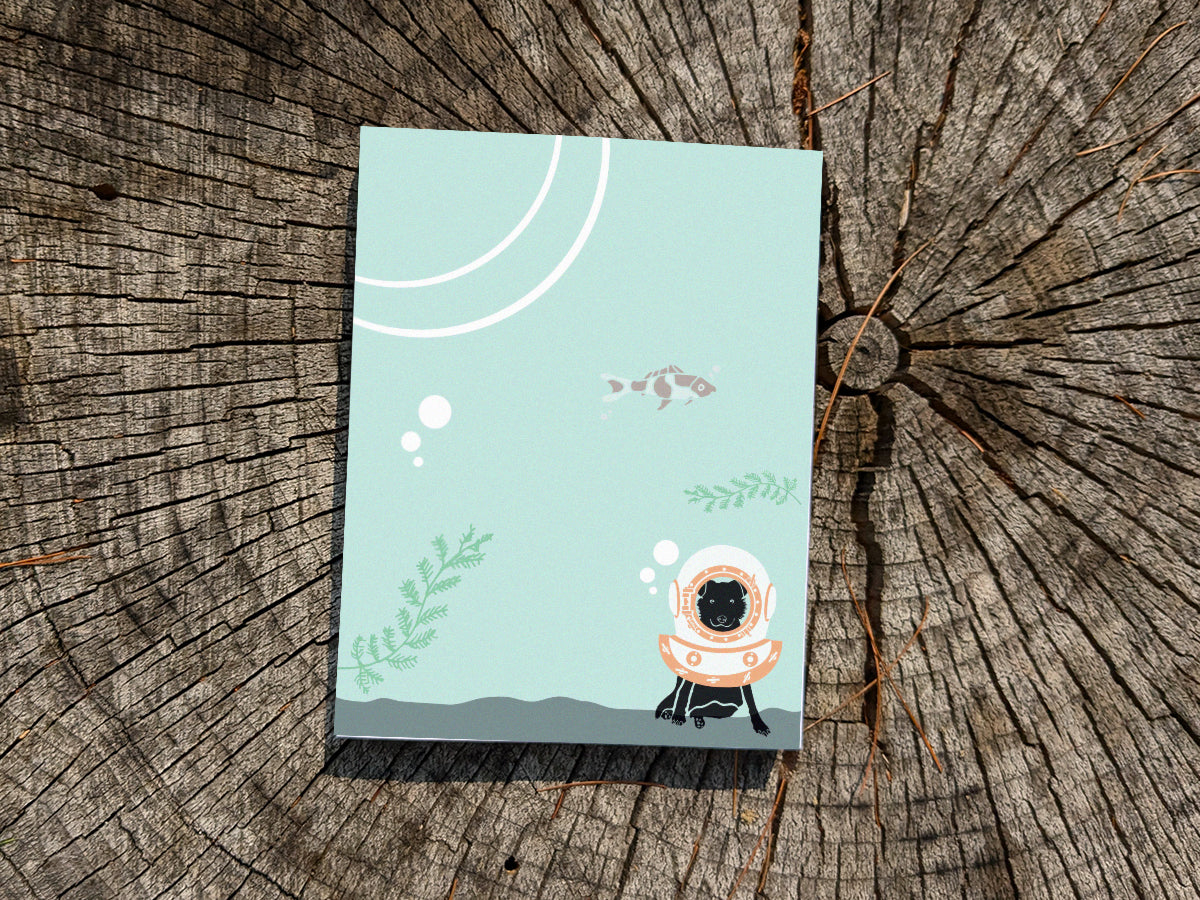 Notepad with a dog with old school diving helmet on a wooden surface.