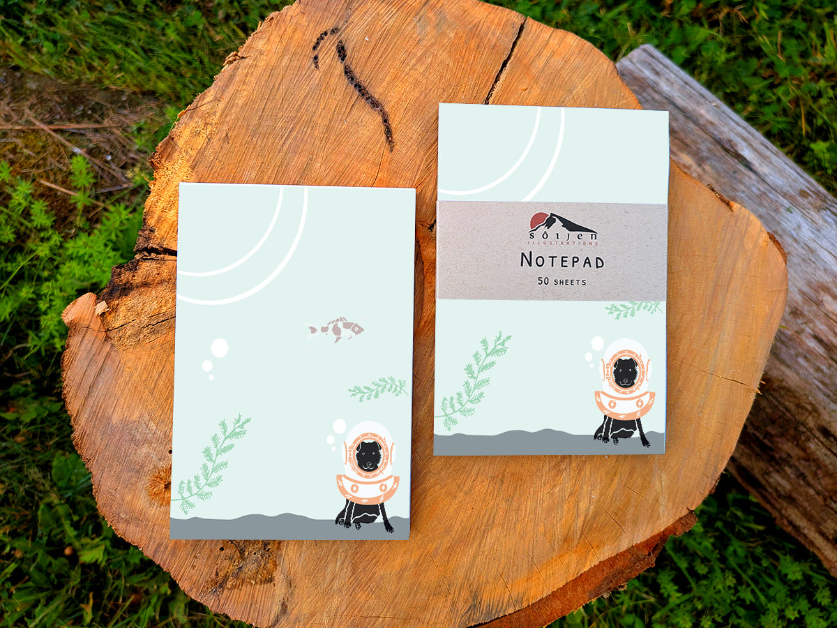 Two notepads with a dog underwater with old school diving helmet and red fish, placed on a wood surface.