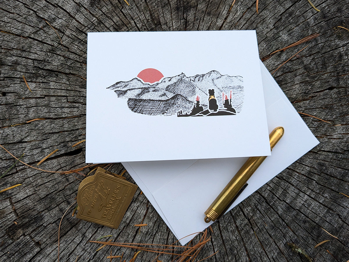 Greeting card with image of black dog looking at a red sunset behind mountains.