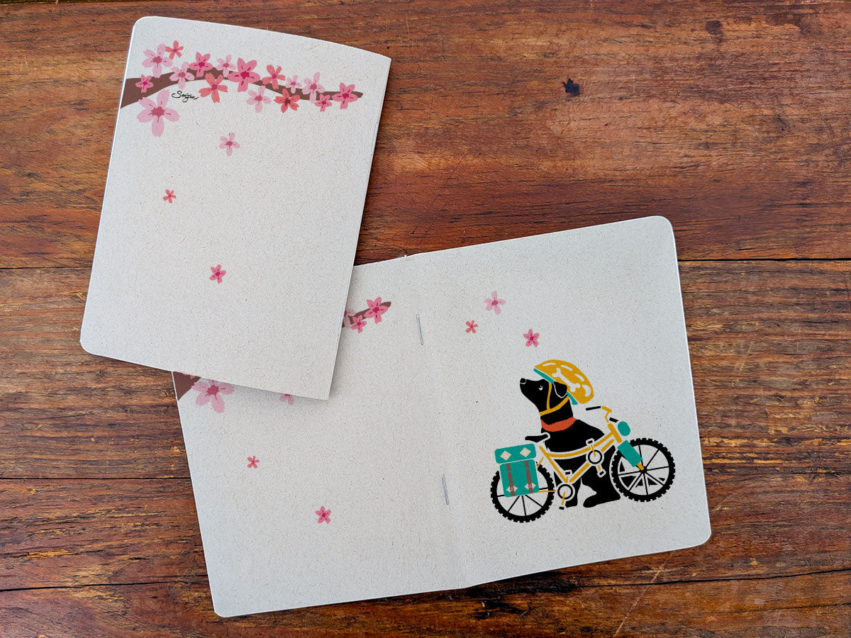 Two notebooks with dog with bicycle illustration on a wooden surface