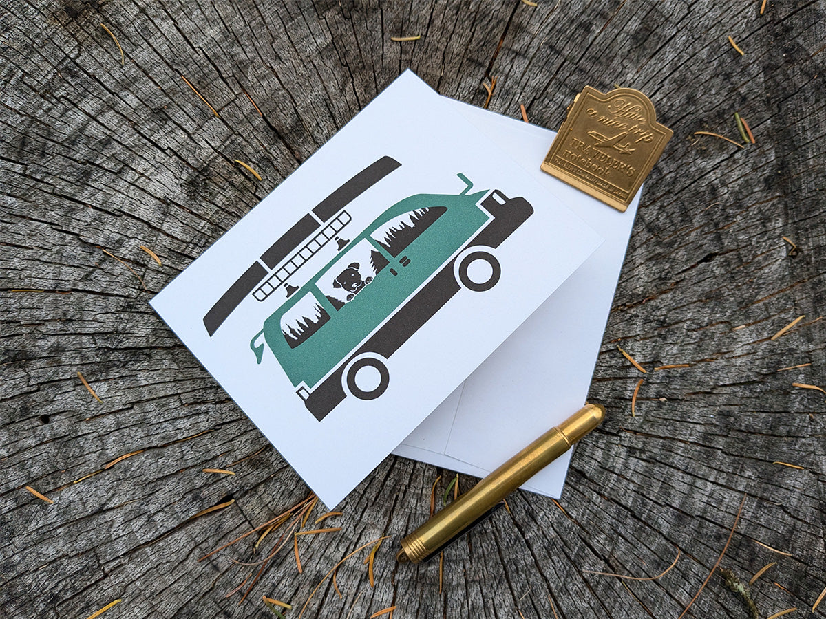 Greeting card with image of dog riding in a camper van with canoe on top.